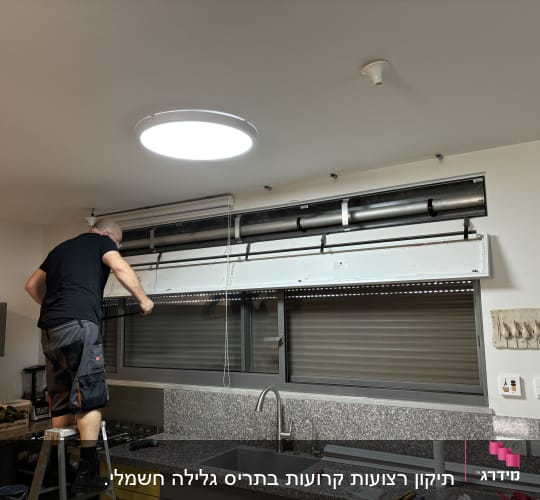 אדם מתקין תריסים חשמליים במטבח על סולם